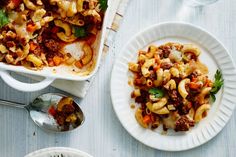 two white plates filled with pasta and meat next to silver spoons on a table