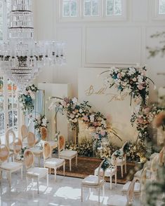 a room filled with lots of white chairs and flowers on the wall next to a chandelier