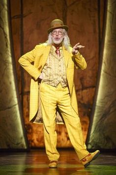 an old man in a yellow suit and hat standing with his hands on his hips