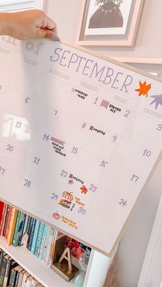 a person holding up a calendar on a book shelf