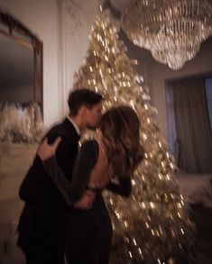 a man and woman are kissing in front of a christmas tree with lights on it