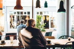 two people sitting at a table in a restaurant looking out the window to the street