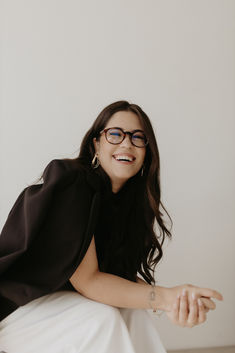 a woman wearing glasses sitting on top of a white chair with her arms outstretched and smiling at the camera