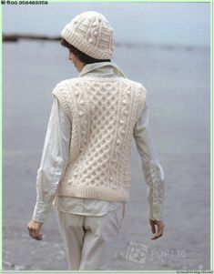 a woman walking on the beach wearing a sweater and hat