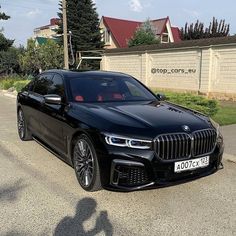 a black bmw is parked on the side of the road in front of a house