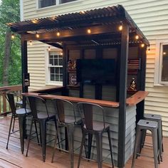 an outdoor bar with stools and lights on the side of it in front of a house