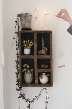 a person lighting a candle on top of a wooden shelf with plants and other items