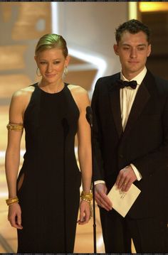 a man in a tuxedo standing next to a woman in a black dress