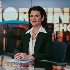 a woman sitting at a desk in front of a news set with the morning show logo behind her