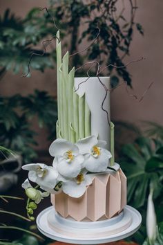 a three tiered cake with white flowers and green leaves on it's side