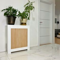 two potted plants sitting on top of a white cabinet next to a door in a living room