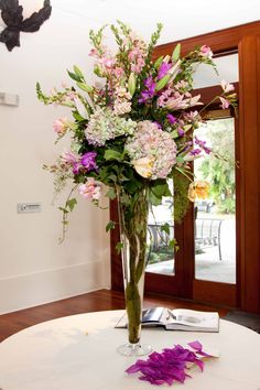 a vase filled with lots of flowers on top of a white table next to a window