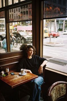 a woman sitting at a table in front of a window looking out on the street