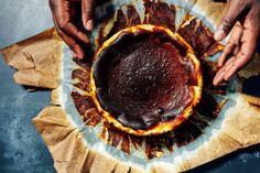 two hands reaching into a chocolate cake on top of wax paper with flames coming out of it