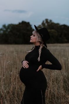 a pregnant woman in a black dress and cowboy hat poses for the camera with her hands on her hips