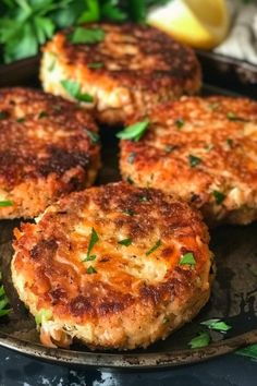 four crab cakes on a plate with lemons and parsley in the back ground