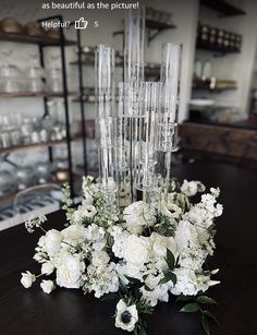 white flowers and greenery are arranged on a table in front of glassware shelves