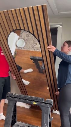 two people standing next to each other in front of a large mirror with wood slats on it