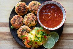 a black plate topped with crab cakes next to a bowl of salsa and lime wedges