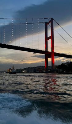 a boat traveling under a suspension bridge at dusk