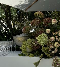 a table topped with lots of wine glasses and flowers next to a vase filled with green grapes