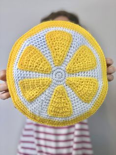 a person is holding up a crocheted lemon cushion in front of their face