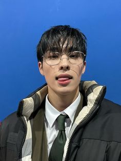 a young man wearing glasses and a green tie is posing for the camera in front of a blue background