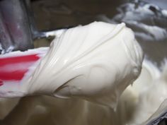 a spoon full of white icing in a metal bowl with red and white spatula