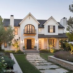 a large white house with lots of windows and plants in the front yard at dusk