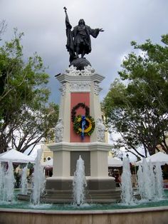 there is a statue with a wreath on it in front of the fountain and trees