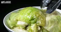 a white bowl filled with lettuce on top of a black table next to a fork