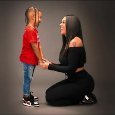 a woman kneeling down next to a little boy who is holding the hand of her