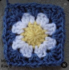 a crocheted square with a yellow and white flower in the center on a gray surface