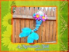 an image of a mermaid tail with flowers on it's head and in the background is a fence