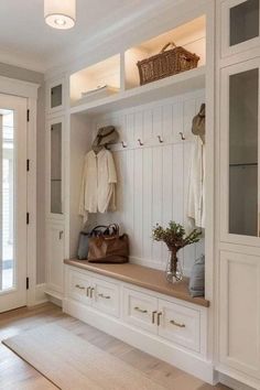 a white entryway with wooden flooring and built - in benches, coat racks, and baskets on the wall