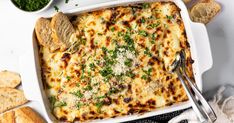 a casserole dish with cheese, bread and parsley in it on a white surface