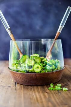 a wooden bowl filled with cucumbers on top of a table next to chopsticks