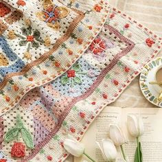 a crocheted blanket with flowers on it next to an open book