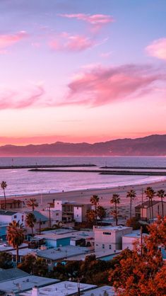 the sun is setting over an ocean with houses and palm trees in front of it