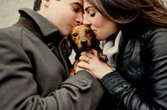 a man and woman kissing while holding a small dog