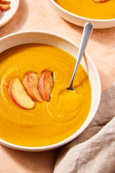 two bowls of soup with apples on top and spoon in the bowl next to them