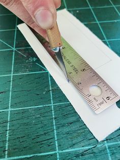 a person is using a ruler to measure the length of a piece of paper on a cutting board