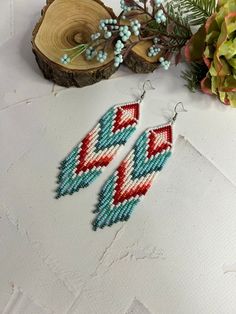 two pairs of beaded earrings sitting on top of a table next to a plant