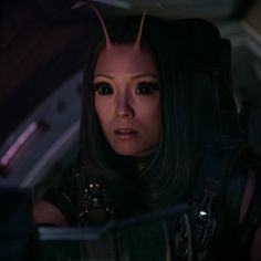 a woman with long black hair and horns on her head sitting in a car looking at the camera