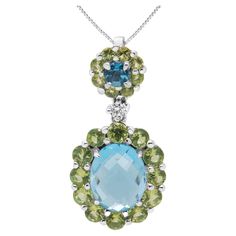 Elegant in its graceful drop design, this pendant necklace sparkles wildly with its collection of diamond and gemstones prong-set into polished 18k white gold. The bail features a center gemstone that is a 3.5mm round blue topaz haled by 2.5mm round peridots. A round white diamond links to the dangle that features a stunning 9.5 x 7.5mm oval blue topaz which is also haloed by green peridots. These are natural, color-treated gemstones for utmost sparkle and shine. The diamond is a total 0.05 cttw Blue Topaz Pendant Necklace, Peridot Pendant, Blue Topaz Pendant, Drop Design, Peridot Gemstone, Green Peridot, Round Cut Diamond, White Diamond, Diamond White