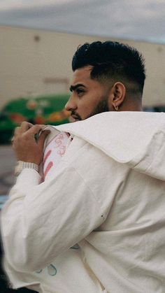 a man in a white jacket is leaning against a car and looking off into the distance