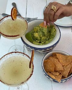 a person dipping guacamole into a bowl with tortilla chips on the side