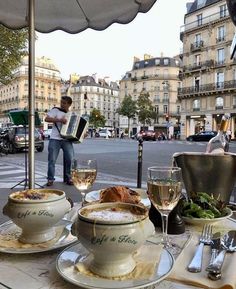 an outdoor dining area with plates, bowls and glasses on the table in front of buildings