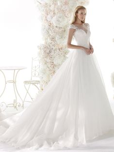 a woman in a white wedding dress standing next to a floral arch with flowers on it