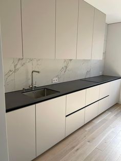 an empty kitchen with white cabinets and black counter tops, along with hardwood flooring